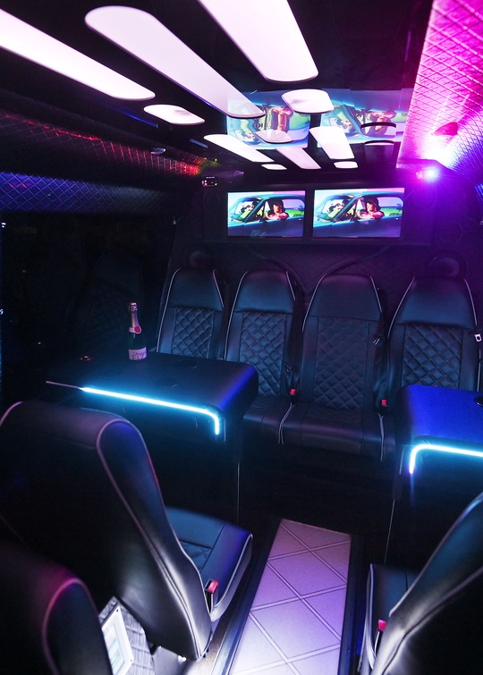 VIP Buses 2010 Mercedes Sprinter 16 Seater Party Bus cabin with tables lit cyan and a bottle on the rear