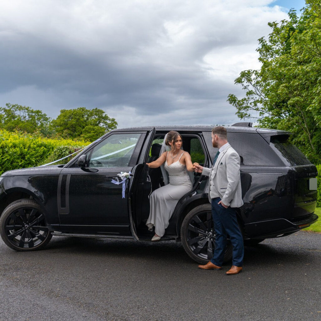 VIP Buses Black Range Rover Vogue SWB with the groom taking the brides hand by a lamp post