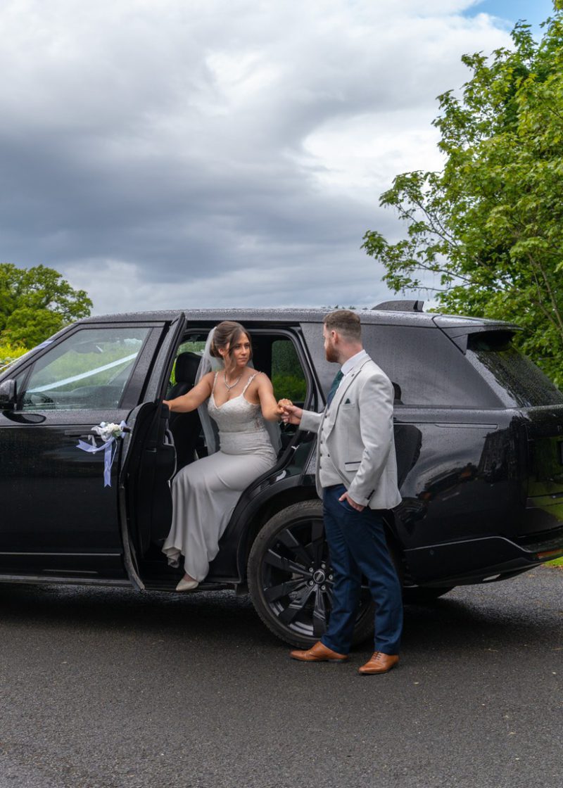 VIP Buses Black Range Rover Vogue SWB with the groom taking the brides hand by a lamp post