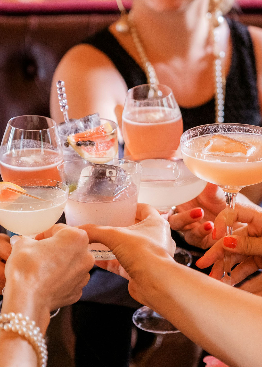 Hen party friends clinking pastel cocktails over a table in a dark booth