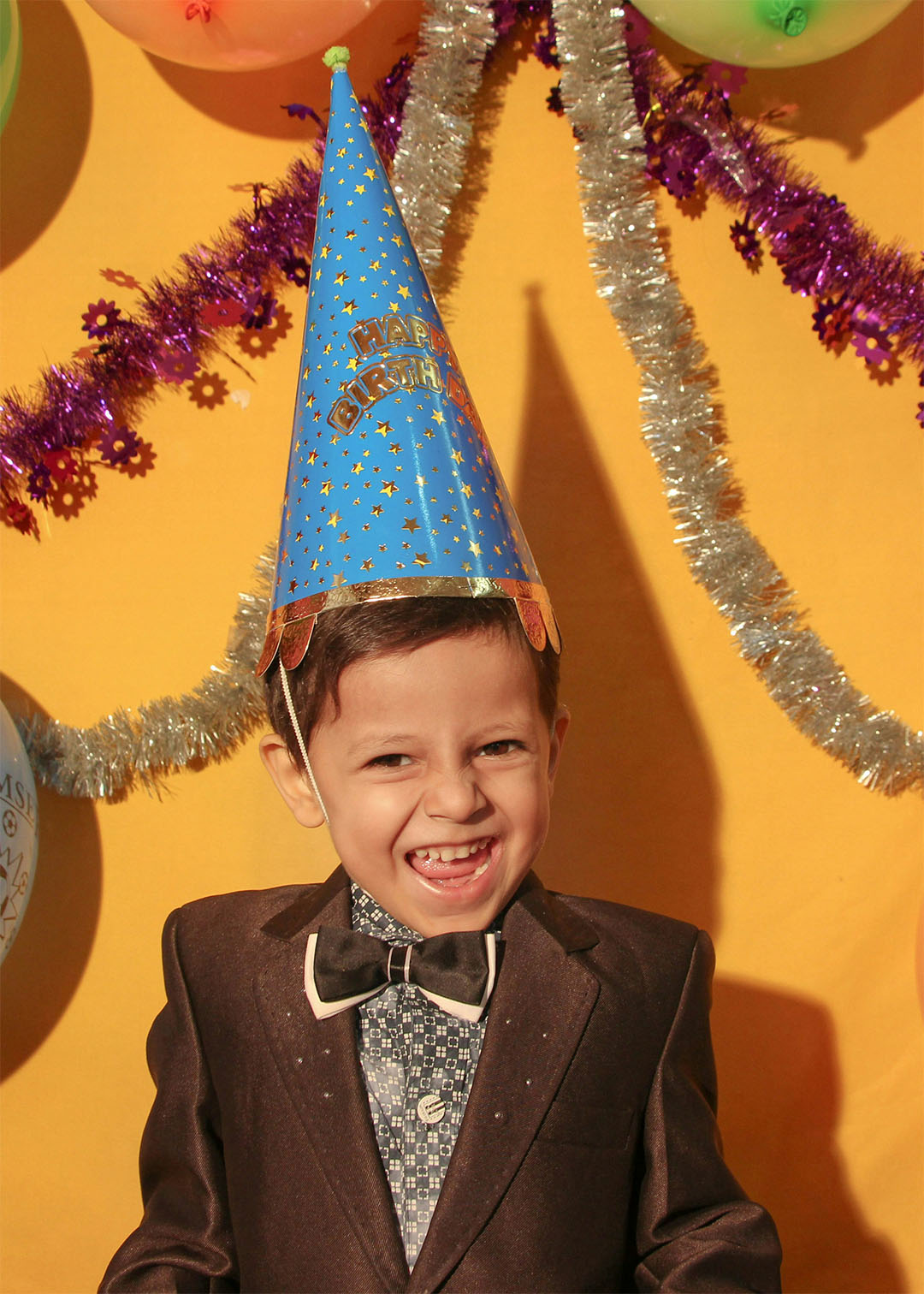 Kids birthday party grinning boy in a suit and party hat under balloons