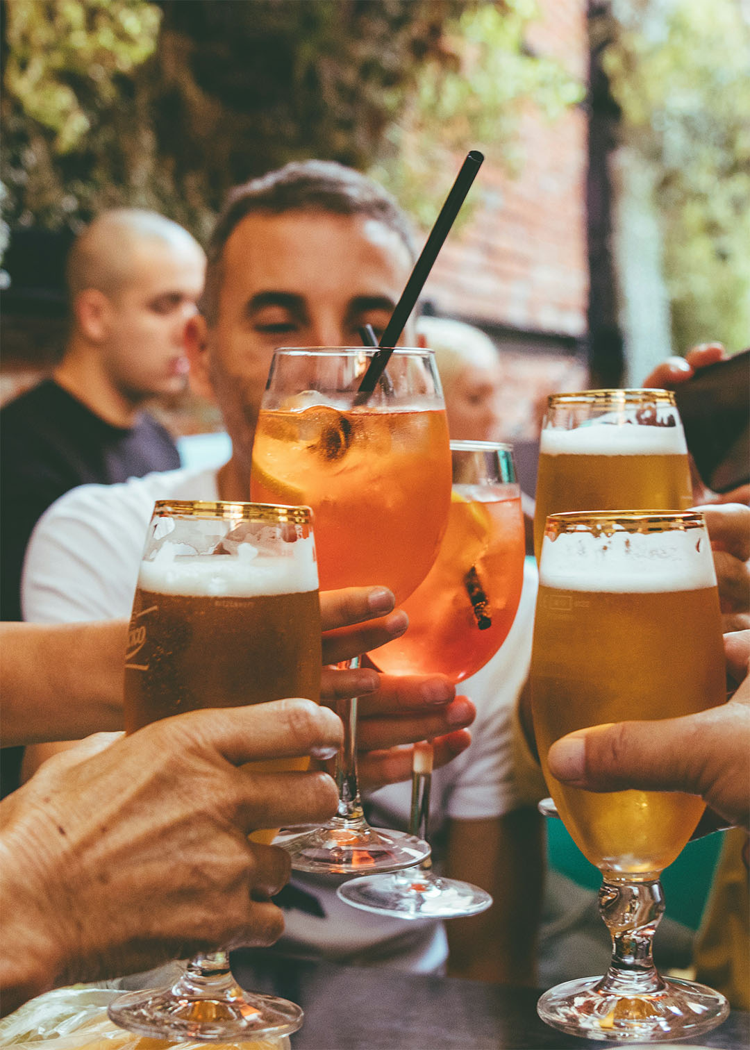 Pub tour friends clinking beers and spritz glasses at an outdoor table