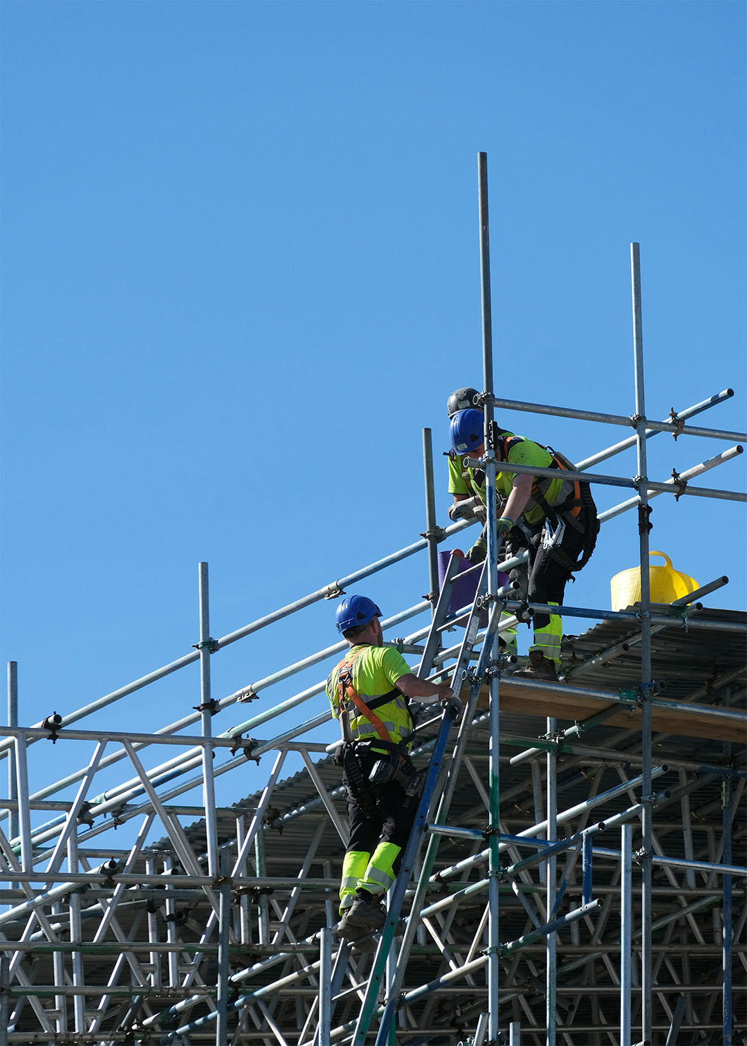 Staff transport scaffolders in hi vis working at height against a blue sky